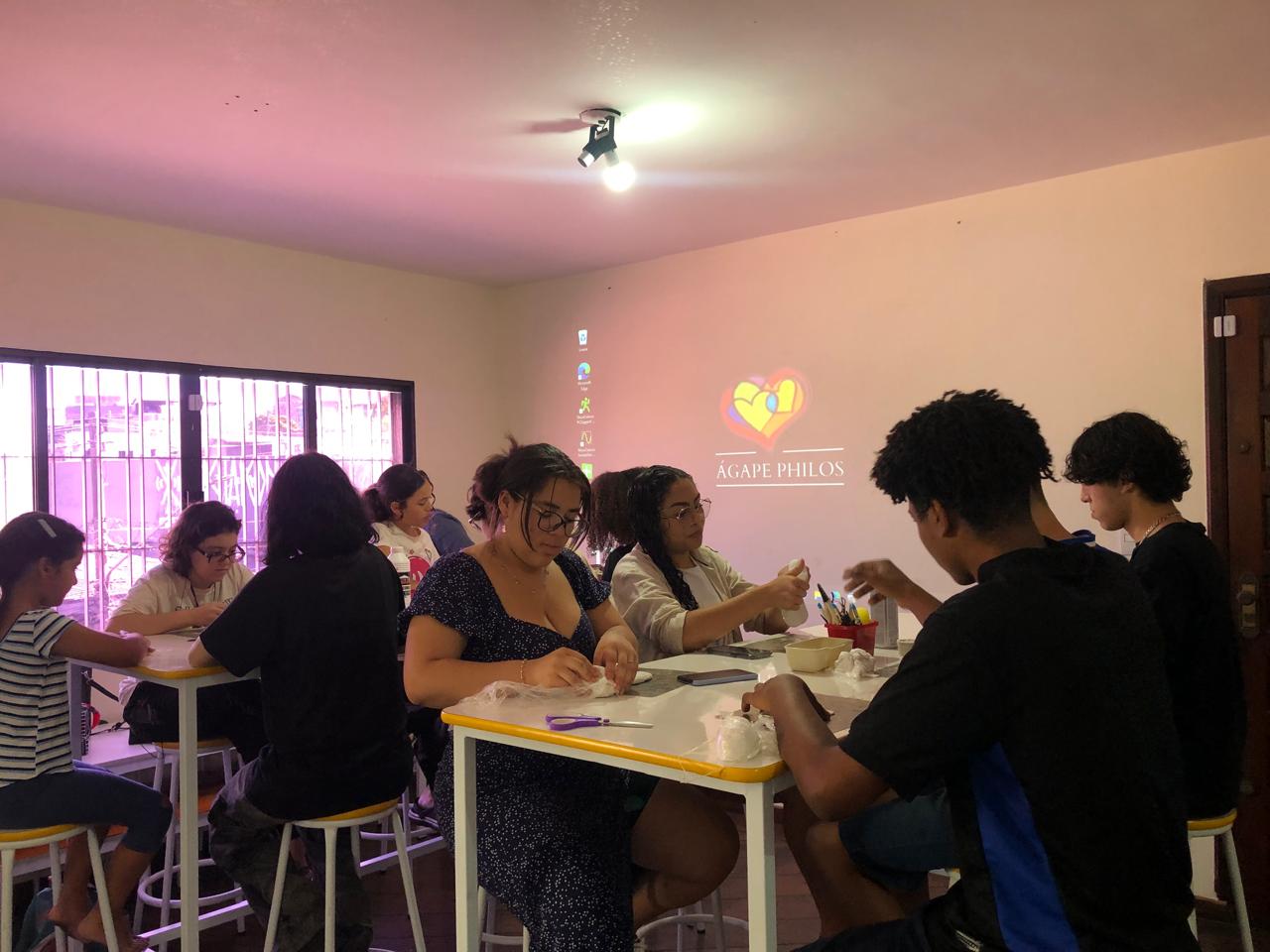 Oficina do Instituto Ágape Philos com participantes em volta da mesa e o logotipo projetado na parede